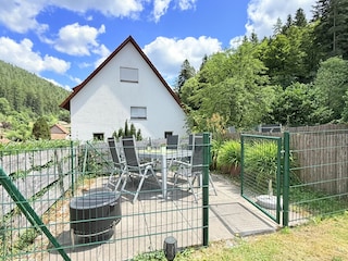 eingezäunte Esstischgruppe mit Grill und Sonnenschirm