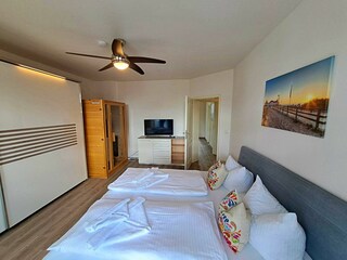 1. Schlafzimmer mit Doppelbett, TV, Kleiderschrank, Infrarotsaunakabine, Zugang zum Balkon