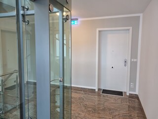 Flur mit Blick zur Wohnungstür und gläserner Fahrstuhl