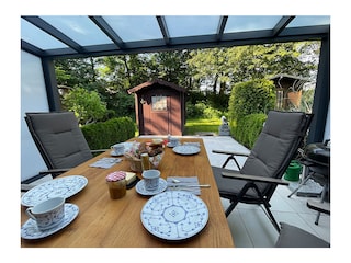 Überdachte Terrasse mit Gartenmöbeln und Grill.