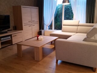 Wohnzimmer mit Couch, Holztisch, Fernseher und  Fenster