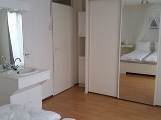 Schlafzimmer mit Badewanne, Holzschränken und Spiegel