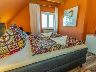 Gemütliches Schlafzimmer mit sichtbaren Deckenbalken, Fernseher und gemütlichem Doppelbett