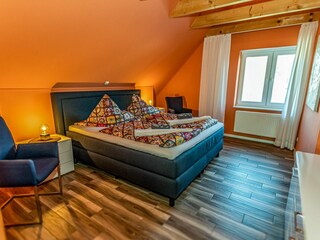 Gemütliches Schlafzimmer mit sichtbaren Deckenbalken, Fernseher und gemütlichem Doppelbett