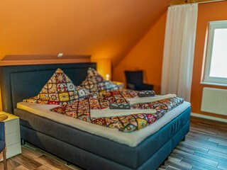 Gemütliches Schlafzimmer mit sichtbaren Deckenbalken, Fernseher und gemütlichem Doppelbett