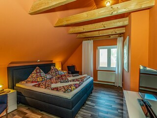 Gemütliches Schlafzimmer mit sichtbaren Deckenbalken, Fernseher und gemütlichem Doppelbett