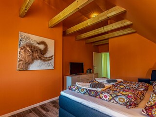 Gemütliches Schlafzimmer mit sichtbaren Deckenbalken, Fernseher und gemütlichem Doppelbett