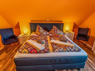Gemütliches Schlafzimmer mit sichtbaren Deckenbalken, Fernseher und gemütlichem Doppelbett