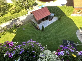 Blick vom Balkon auf den Garten mit Gartenhaus und Grill.