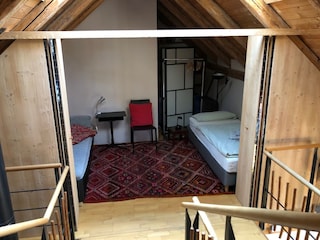 Doppel-Schlafsofa und Einzelbett hinter Holz-Falttür