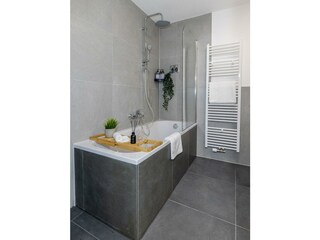 Dusche und Badewanne mit Badebrett und Regndusche.