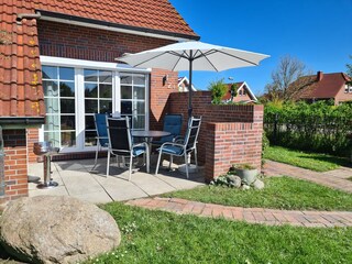Windgeschützte Terrasse mit Tisch, Stühlen und Grill