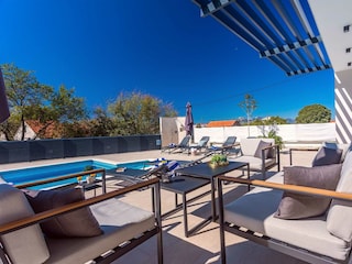 Rund um den Pool stehen acht Liegestühle.