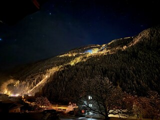 Haus in der Nacht mit beleuteter Rodelpiste