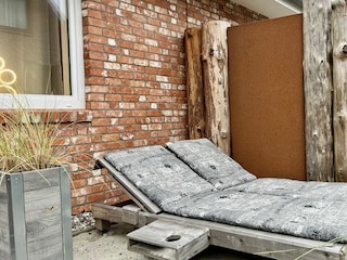 Holzliegen im Garten mit Auflagen und Getränkeablagen