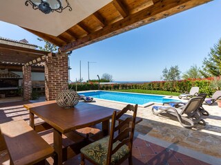 Covered outdoor eating area with BBQ next to the pool