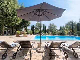 Sonnenliegen, Sonnenschirm und Bäume neben dem Pool