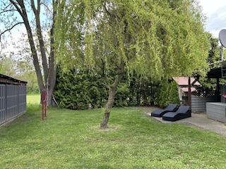 Blick in den umzäunten Garten mit Sonnenliegen