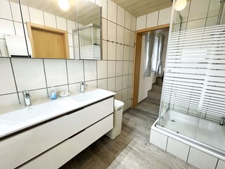 Badezimmer mit Doppelwaschtisch und großer Dusche.